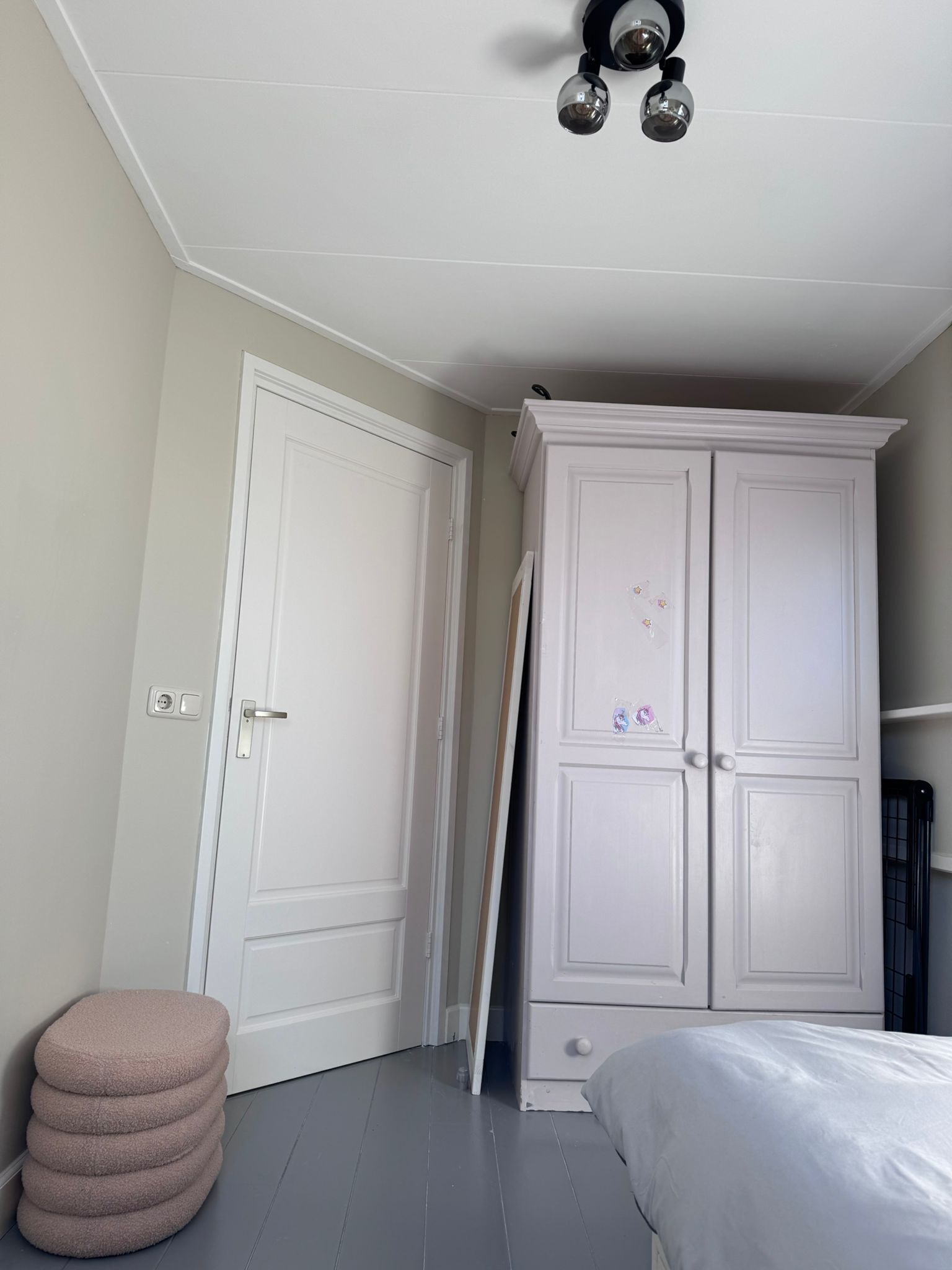 A bedroom with a white wardrobe, a bed, a small stool, and a ceiling fan.