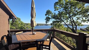 A wooden deck with a table and chairs, overlooking a lake.