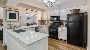 A modern kitchen with white cabinetry, a black refrigerator, a microwave, and a stove. There is a granite countertop and a sink.