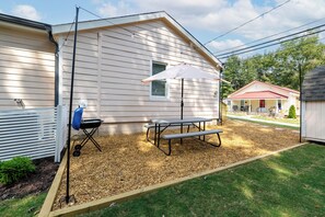Un espace extérieur abrité, doté d’une table de pique-nique et d’un barbecue, entouré d’une terrasse en bois et d’une pelouse.