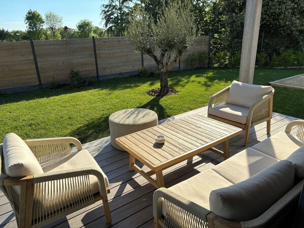 Une terrasse extérieure avec des meubles en osier, une table en bois et un petit arbre.