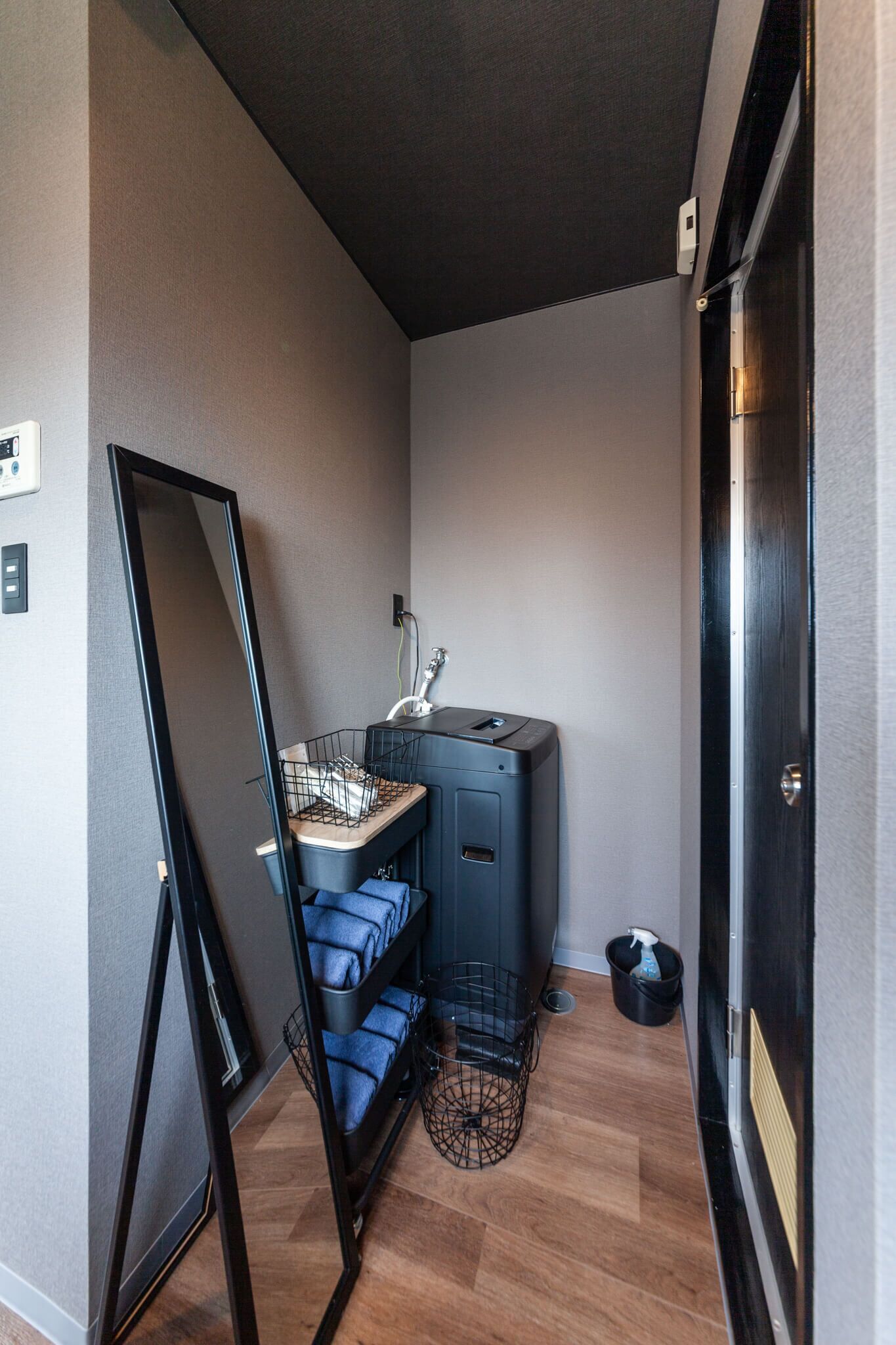 A compact room with a dark ceiling, a large mirror, a small desk with a lamp, and a blue chair.