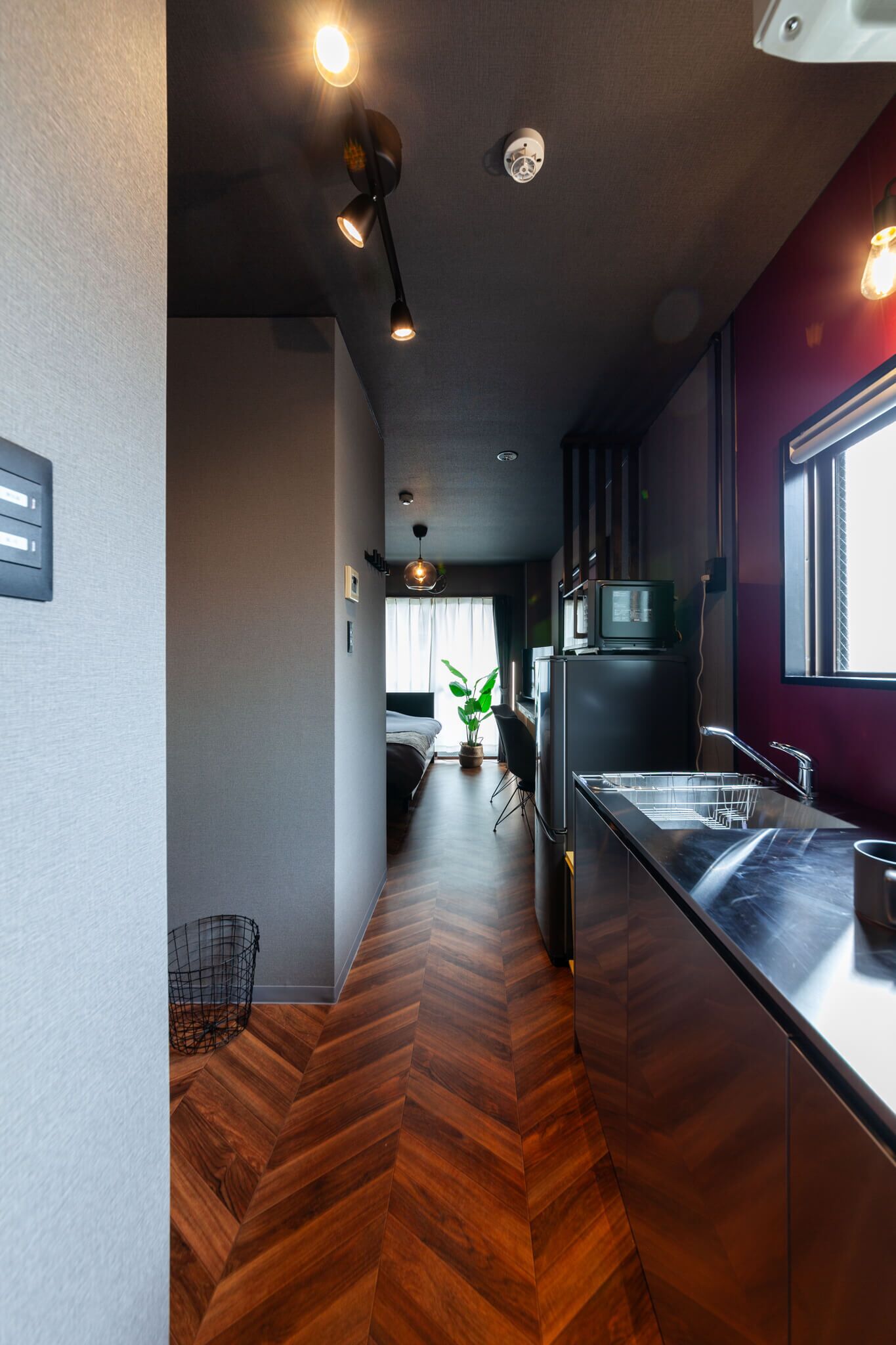 Cozinha moderna com piso de madeira em padrão herringbone, geladeira embutida e janela que permite entrada de luz natural.