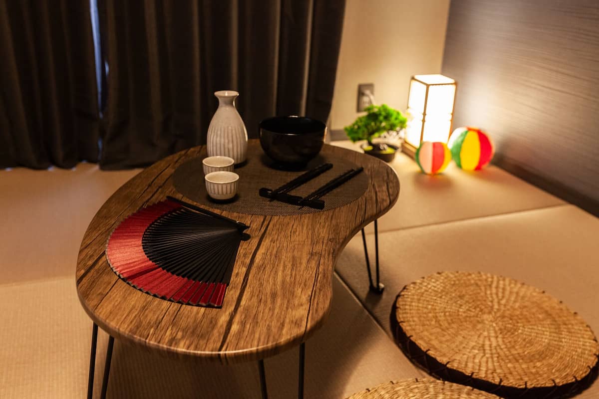 Una mesa de madera con un ventilador, un cuenco negro y un florero blanco.