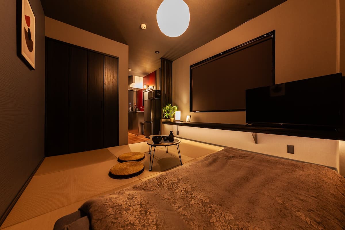 Una habitación pequeña con cama, televisor, una mesita con una planta y un futón.