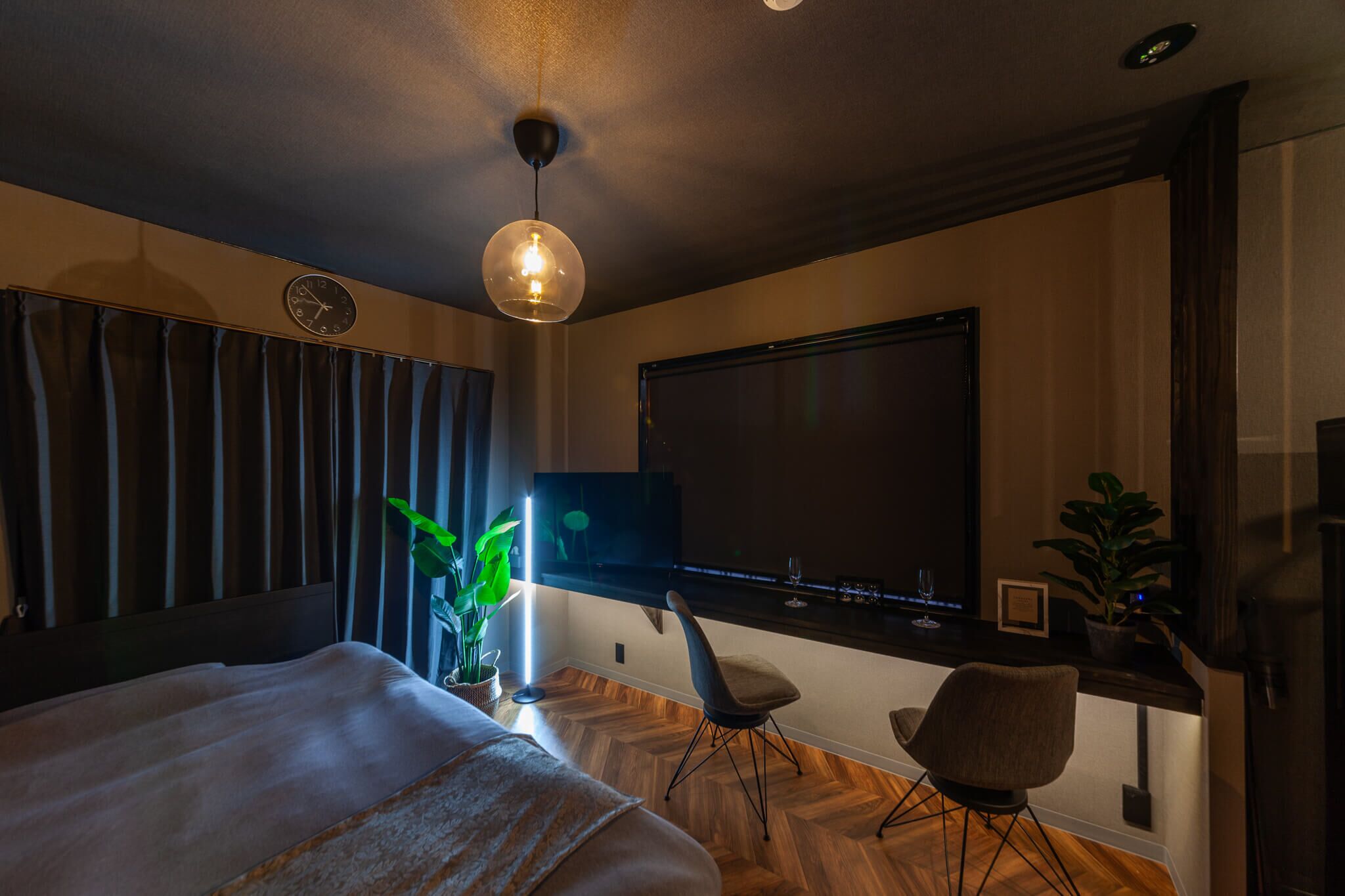 A modern hotel room with a large bed, a desk with a chair, a TV, and a potted plant.