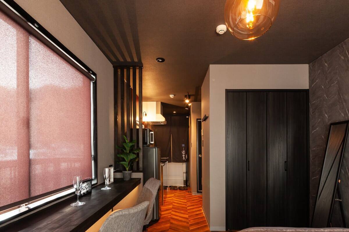 Habitación de hotel moderna con piso de madera en patrón de espiga, un ventanal grande, un escritorio con silla, una cama y una lámpara colgante original.