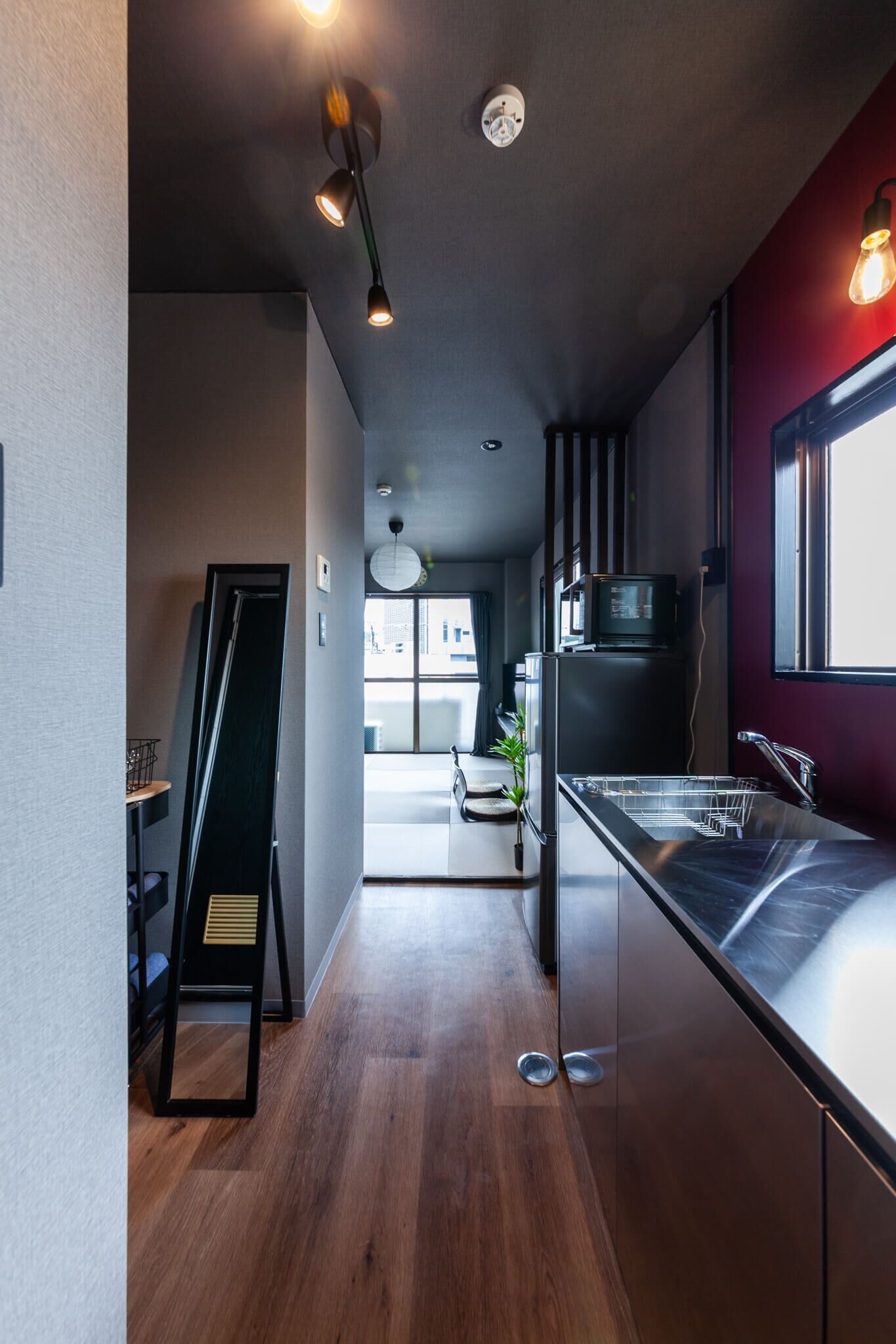 A modern kitchen with a stainless steel sink, a microwave, and a refrigerator. There is a wooden floor and a black chair in the background.