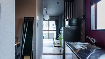 A modern kitchen with a stainless steel sink, a microwave, and a refrigerator. There is a wooden floor and a black chair in the background.