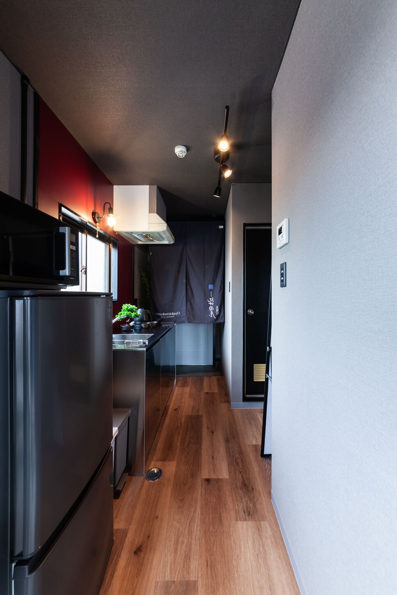 A modern kitchen with a stainless steel refrigerator, a microwave, and a stove. There is a wooden floor and a dark curtain in the background.
