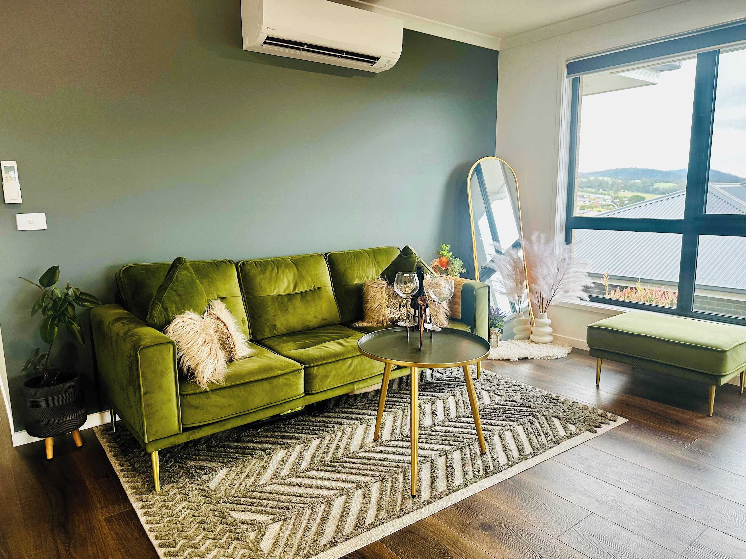 A green sofa, a round coffee table, a large window with a view, and a mirror.