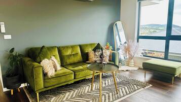 A green sofa, a round coffee table, a large window with a view, and a mirror.