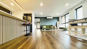 A modern living room with a wooden floor, a green sofa, a dining table, and a kitchen area with a bar stool.