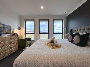 Une chambre à coucher moderne, dotée d’un grand lit, d’une télévision, d’une commode et offrant une vue sur l’extérieur grâce à trois fenêtres.