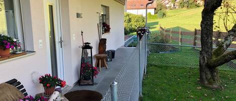 A covered porch with a metal railing, potted plants, and a wooden bench.