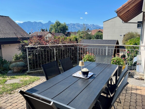 An outdoor patio with a table and chairs, a metal railing, and a view of mountains.