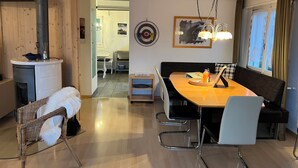 Una habitación acogedora con techo de madera, una mesa de comedor con sillas, un sofá, una chimenea y una ventana con cortinas.