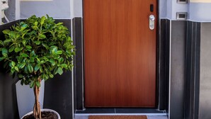 A modern building entrance with a wooden door, a potted plant, and a welcome mat. - MEDUSA CILEA GUEST HOUSE (Naples)