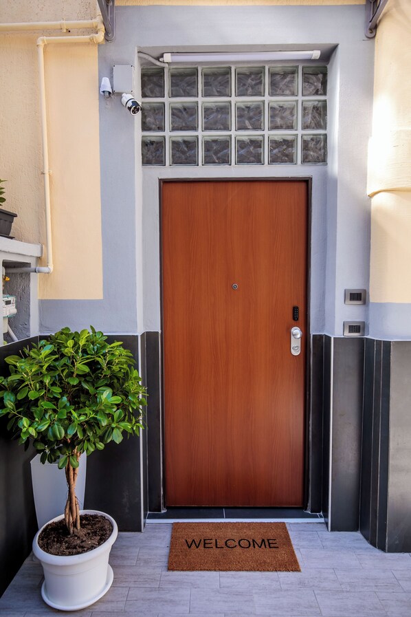 A modern building entrance with a wooden door, a potted plant, and a welcome mat. - MEDUSA CILEA GUEST HOUSE (Naples)