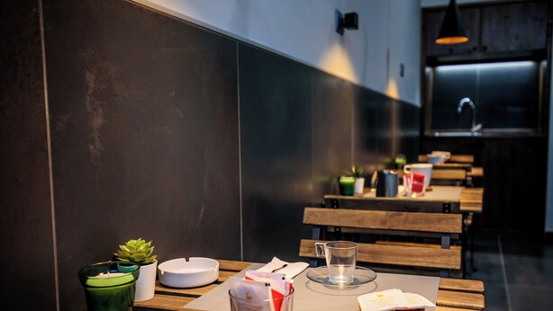 A clean, modern dining area with wooden tables and benches, a green potted plant, a candle, and a glass pitcher. - MEDUSA CILEA GUEST HOUSE (Naples)