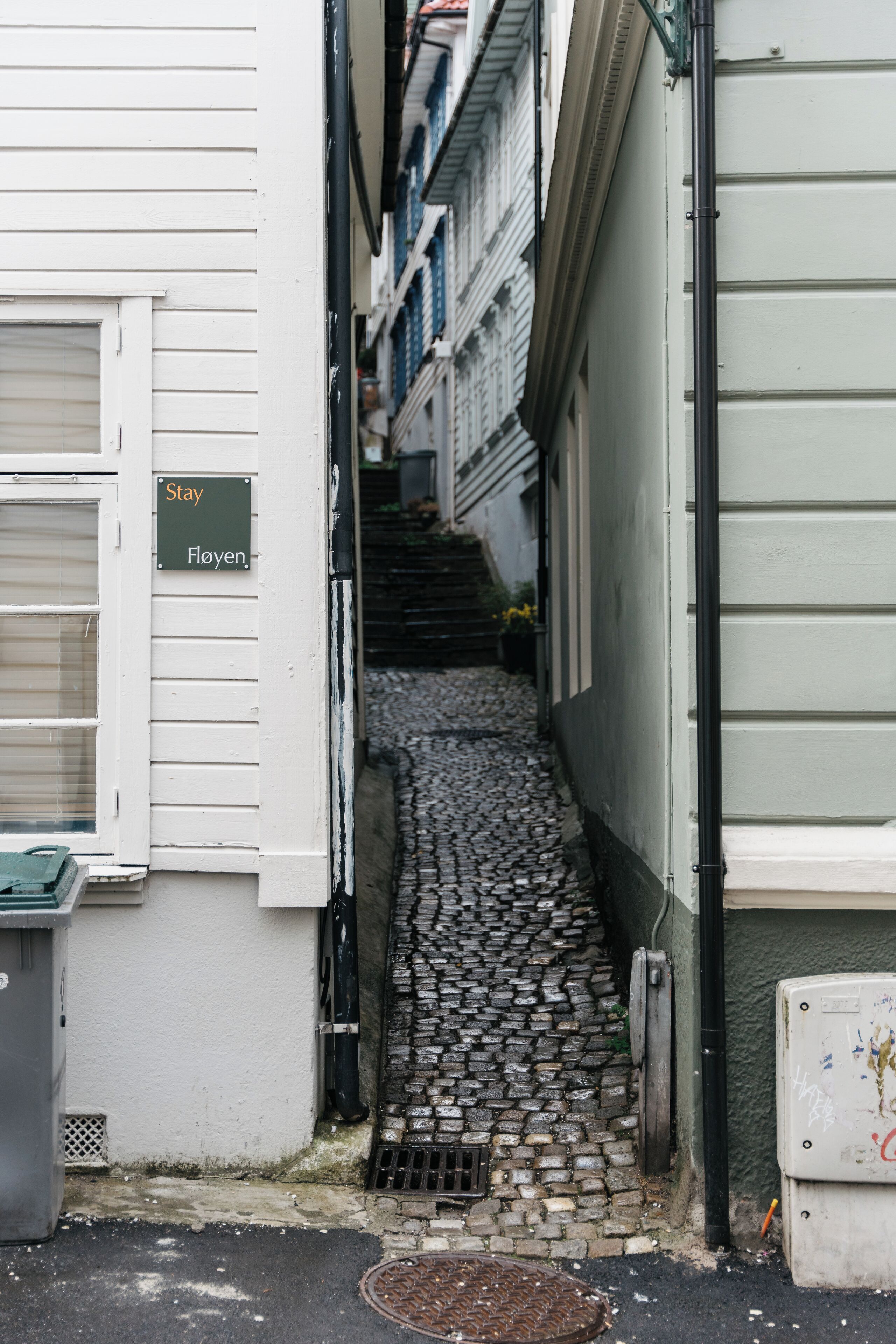 A narrow cobblestone alleyway between buildings with a 'Stay' sign on the left.