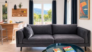 A modern living room with a grey sofa, a glass coffee table, and a view of a mountainous landscape through large windows. - New Villa Sea and Mountain View - Calenzana, near Calvi  (Calenzana)