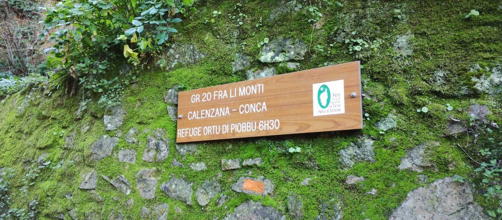 Une plaque en bois portant un texte et un logo, fixée sur un rocher recouvert de mousse.
