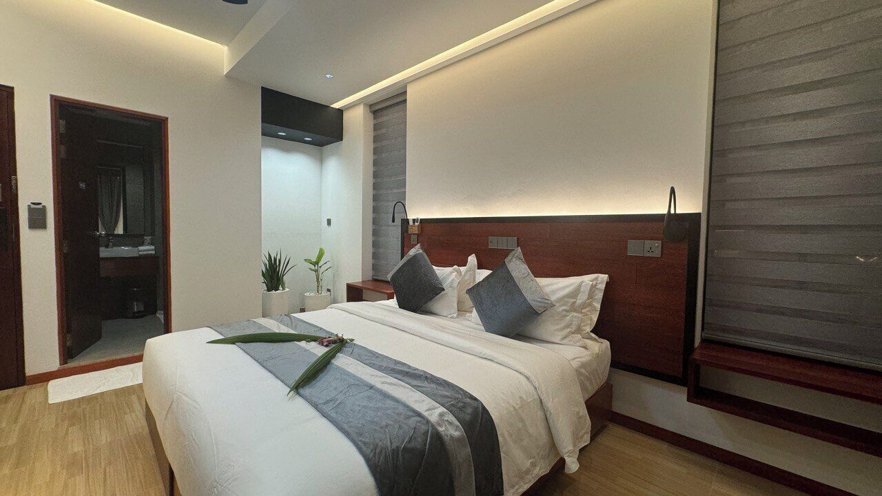 Moderni hotellihuone, jossa on suuri sänky, yöpöytä, pieni sivupöytä, ruukkukasvi ja liukuovi.