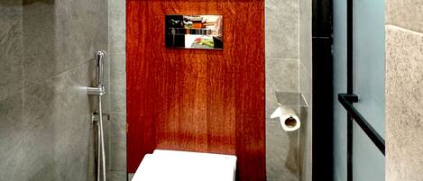 A modern bathroom with a white toilet, a stainless steel trash bin, and a shower area.