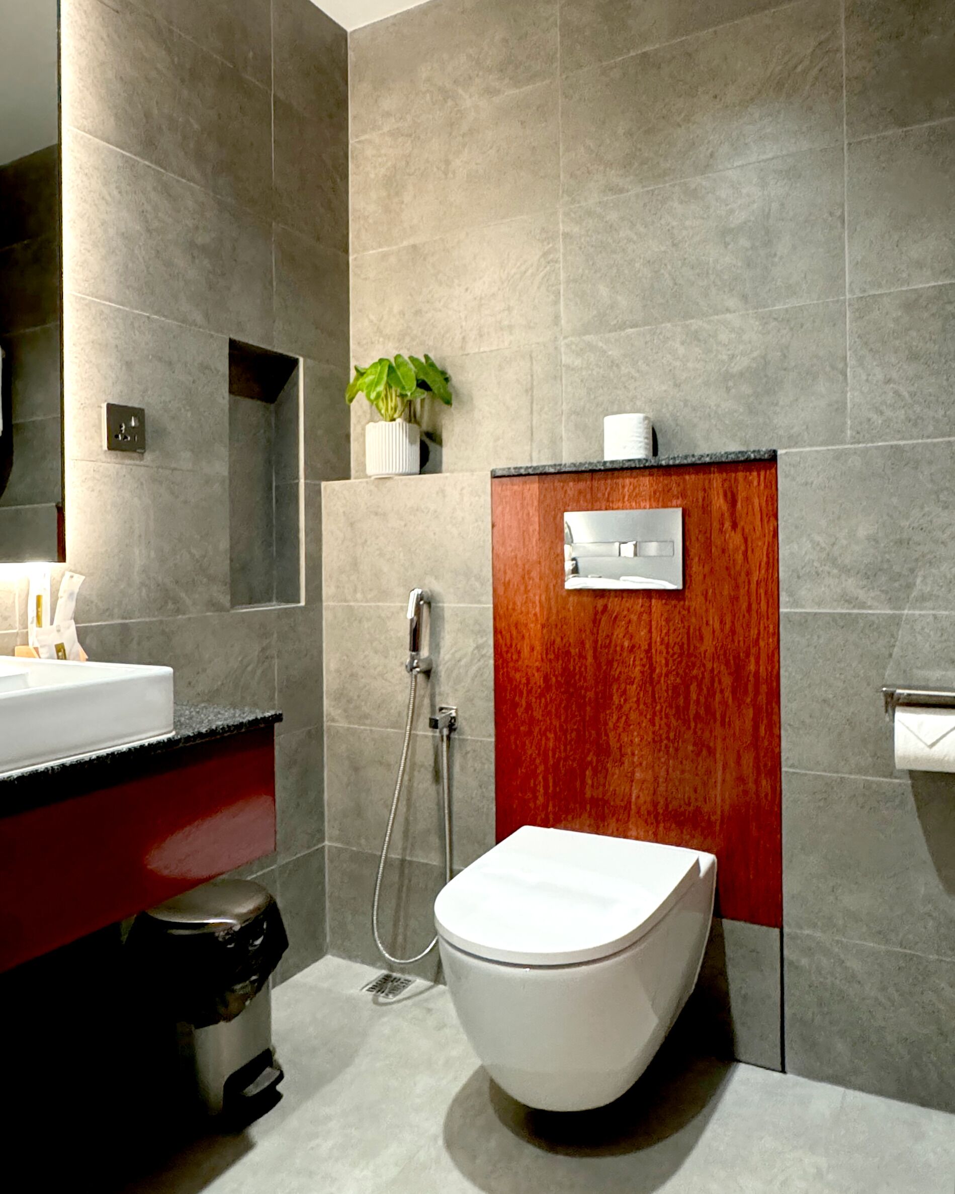 A modern bathroom with a white toilet, a red vanity, a sink, and a shower.