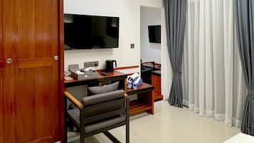Een moderne hotelkamer met een houten deur, een flatscreen televisie aan de wand, een bureau met stoel, een bed en een groot raam met grijze gordijnen.