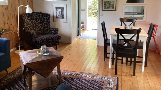 A cozy living room with a patterned armchair, a dining table with chairs, and a small coffee table. - 6 Person Holiday Home in Henan (Henån)