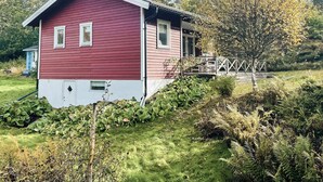 A red house with a white lower section, surrounded by greenery and a wooden bridge. - 6 Person Holiday Home in Henan (Henån)