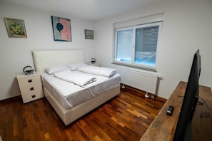 A bedroom with a bed, a nightstand, a desk with a computer, a window with blinds, and a radiator. - Luxury Villa Lucca in Feričanci (Fericanci)