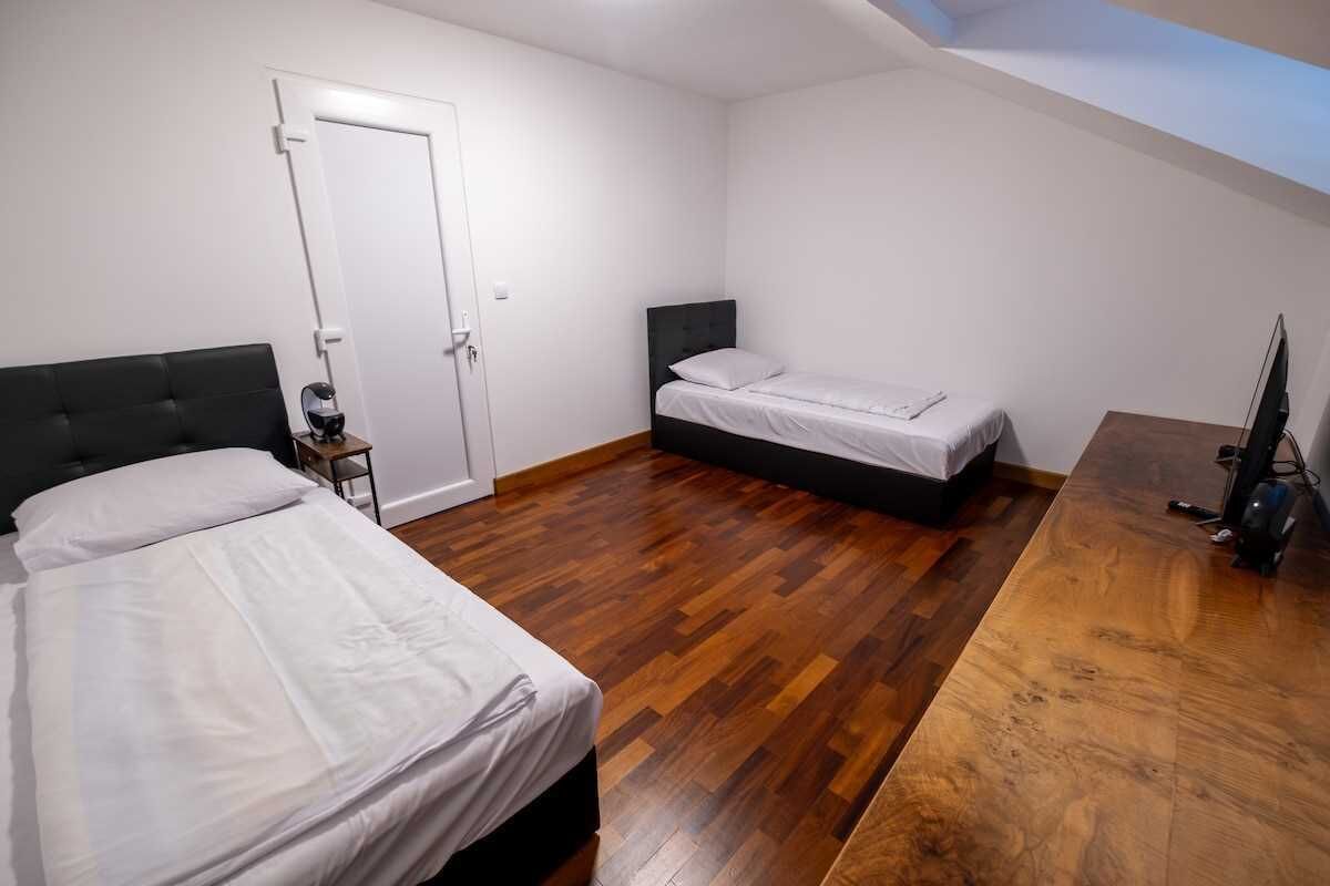Ein Schlafzimmer mit zwei Betten, Holzboden, einer weißen Tür und einem Fernseher auf einem Holztisch.