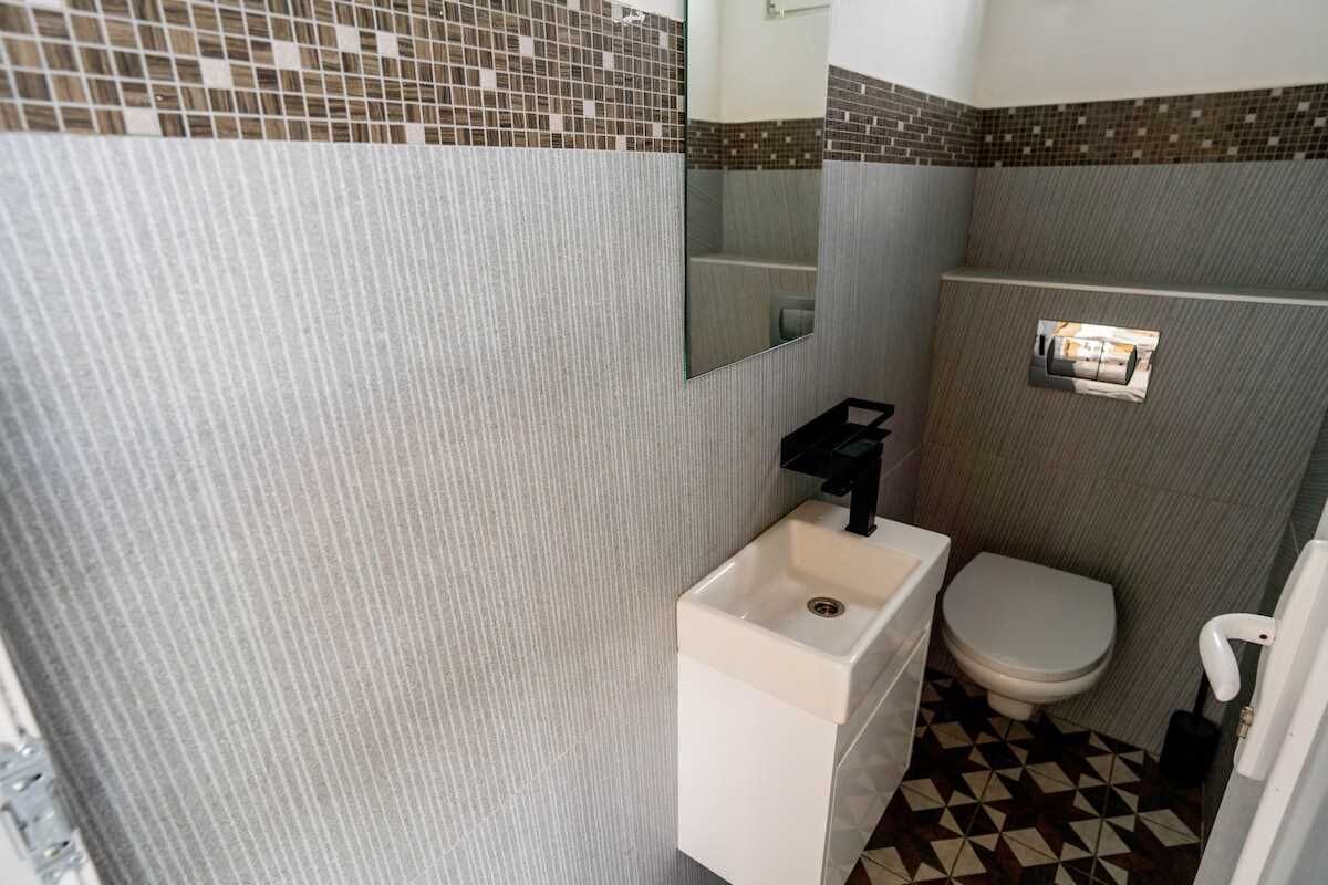 A bathroom with a tiled floor, a white sink, a toilet, and a mirror.