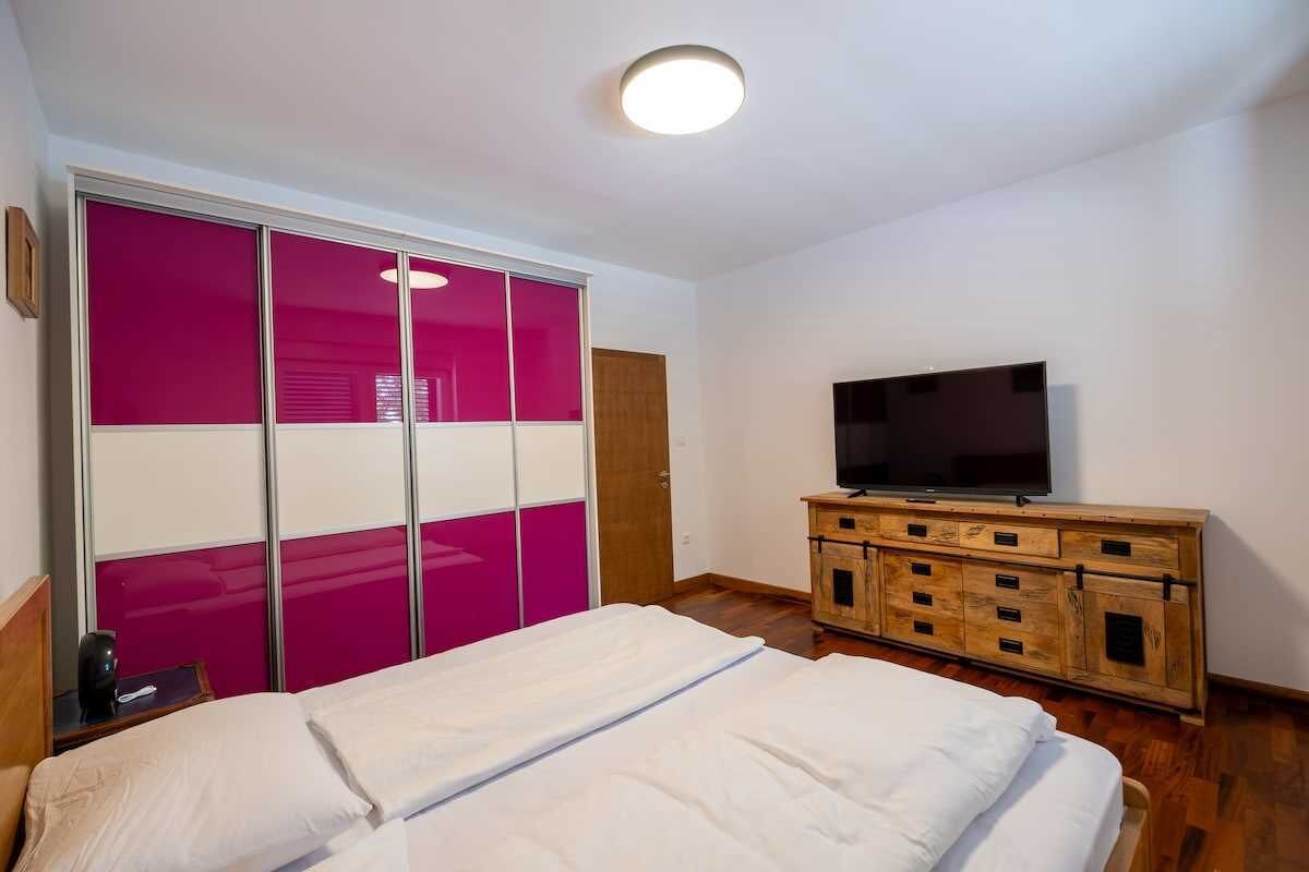 A bedroom with a bed, a TV on a wooden dresser, and a sliding door with pink panels.
