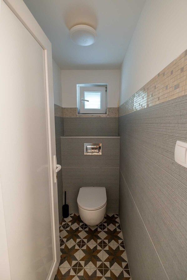 A small bathroom with a toilet, a window, and a tiled floor. - Luxury Villa Lucca in Feričanci (Fericanci)