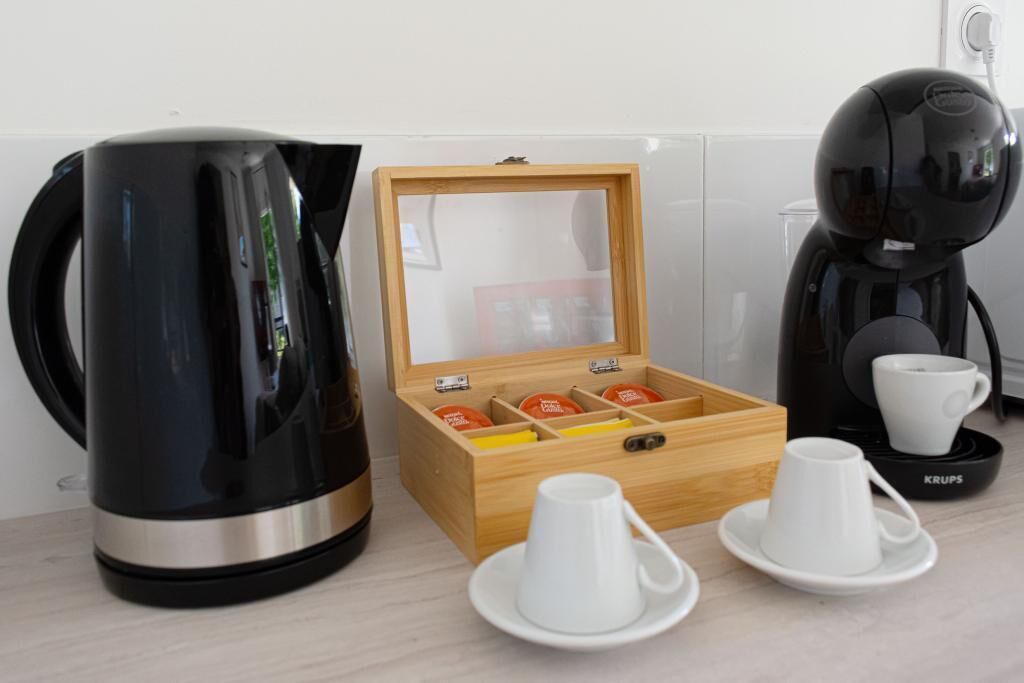 A coffee station with a black coffee maker, a wooden box with tea bags, and white cups and saucers.