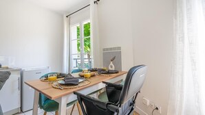 Een eethoek met een tafel voor twee personen, een stoel, een kleine koelkast en een raam met gordijnen.