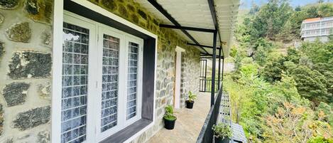 A stone building with a balcony, white-framed windows, and potted plants.