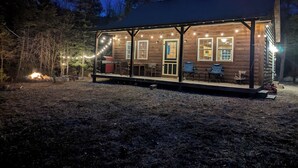 Uma cabana de madeira com varanda, luzes de festa e churrasqueira.