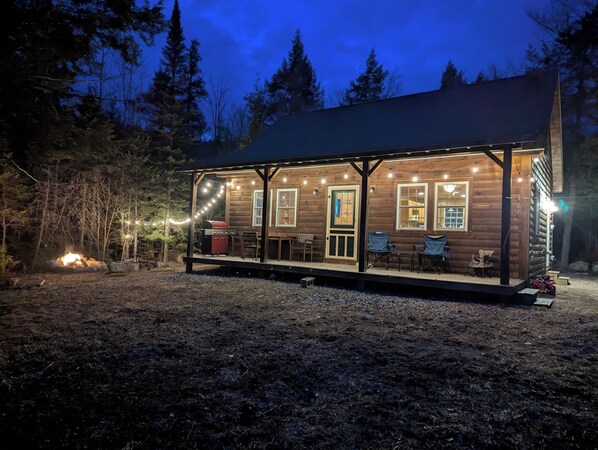 A wooden cabin with a porch, string lights, and a grill.