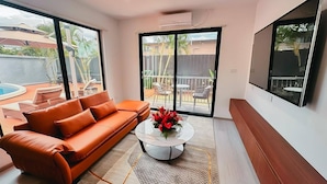 A modern living room with a leather sofa, a glass coffee table with flowers, and a large sliding glass door leading to a balcony with outdoor furniture. - Hibiscus Suites And Residences  (Nadi)