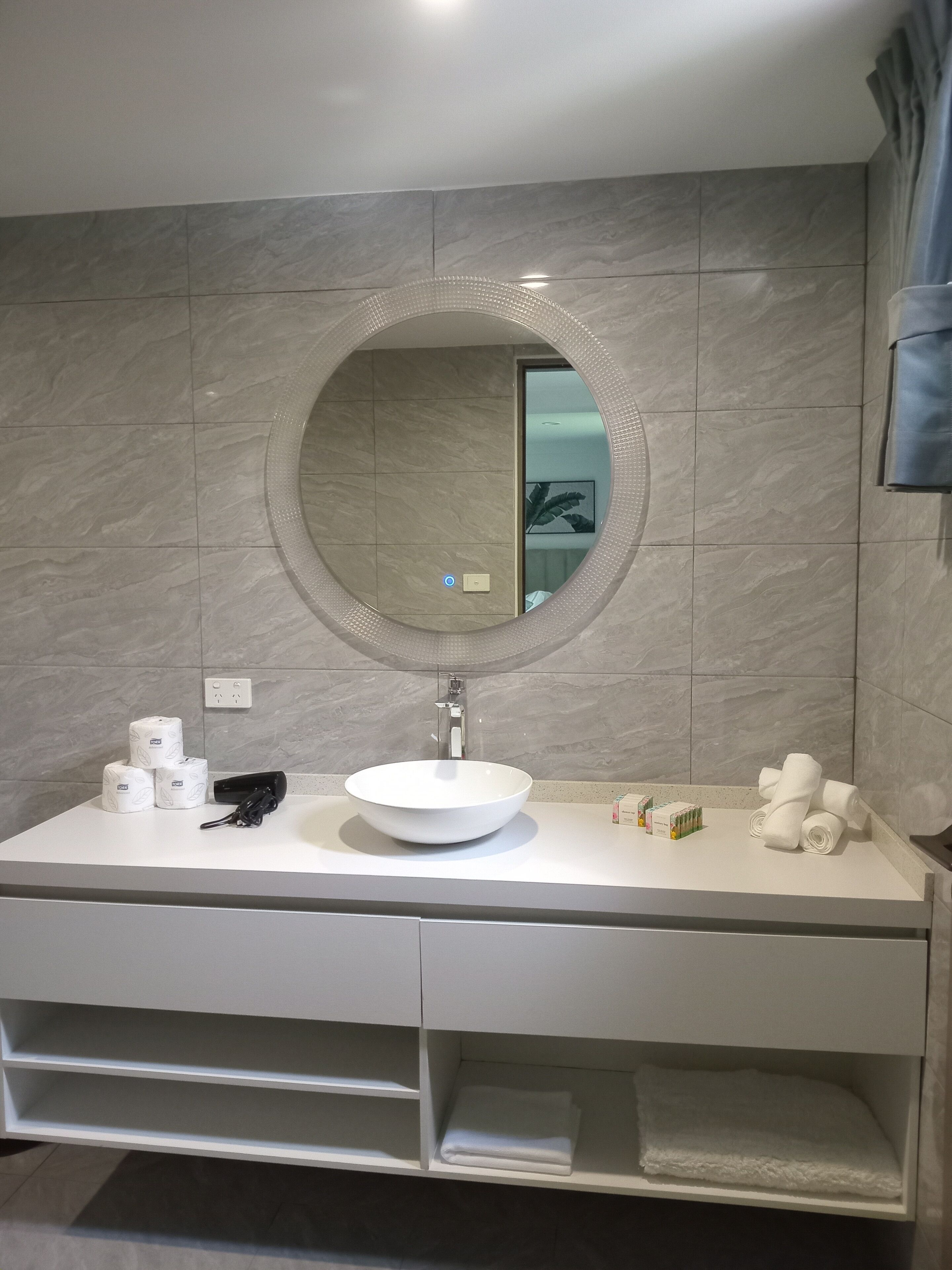 A bathroom with a round mirror, a white sink, and a vanity with storage drawers.