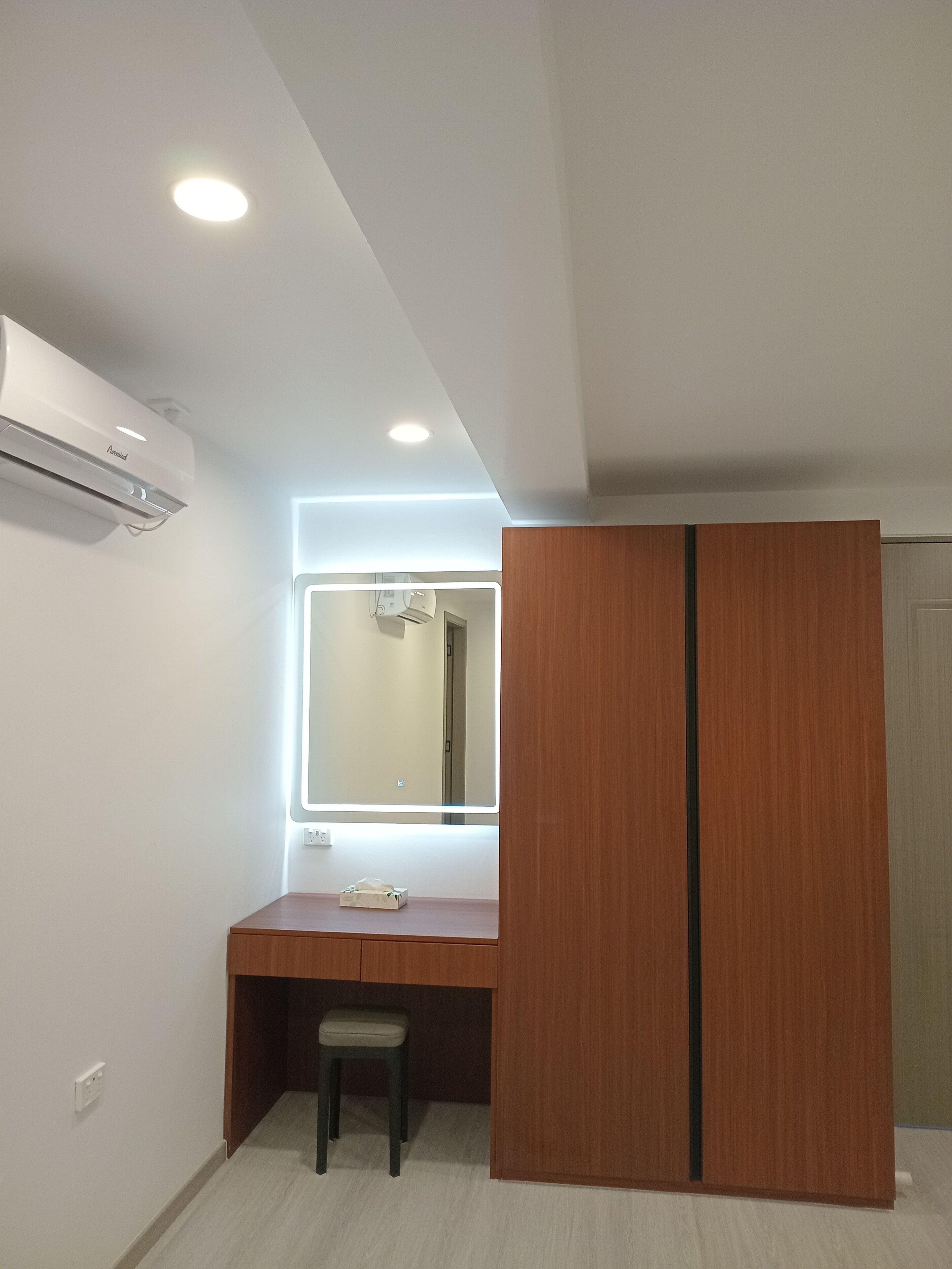 A small, modern room with a wooden desk, a mirror with backlighting, and a wardrobe.