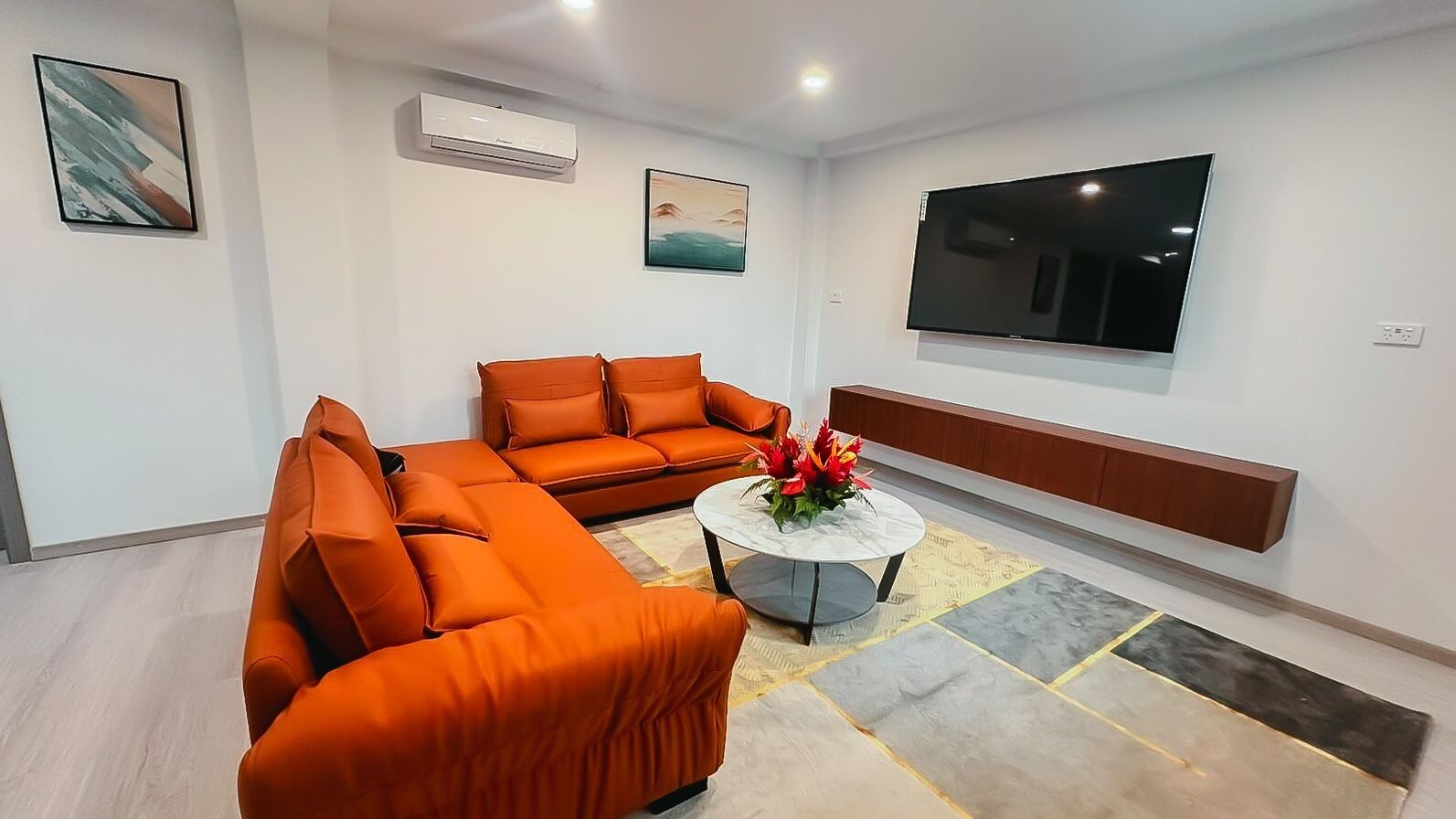 A modern living room with a sectional sofa, a round coffee table, and a flat-screen TV mounted on the wall.