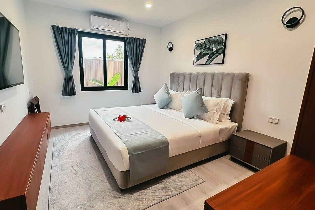 A bedroom with a bed, a bedside table, a TV, and a window with curtains.