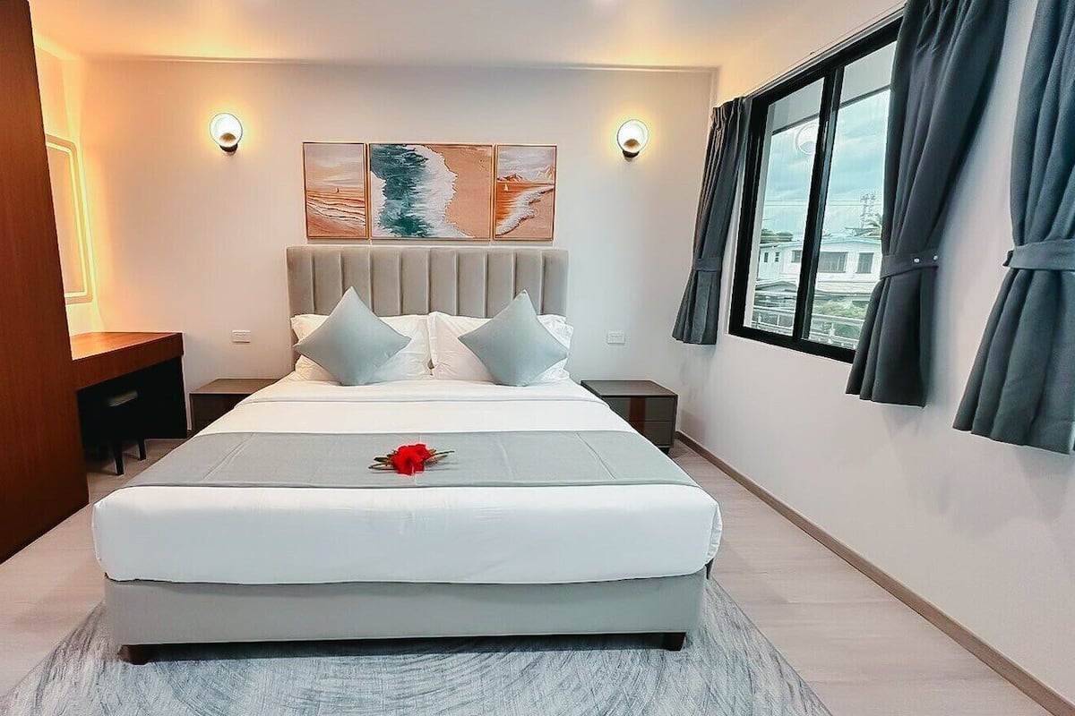 A modern hotel room with a large bed, a nightstand, a wall-mounted light, and a window with curtains.