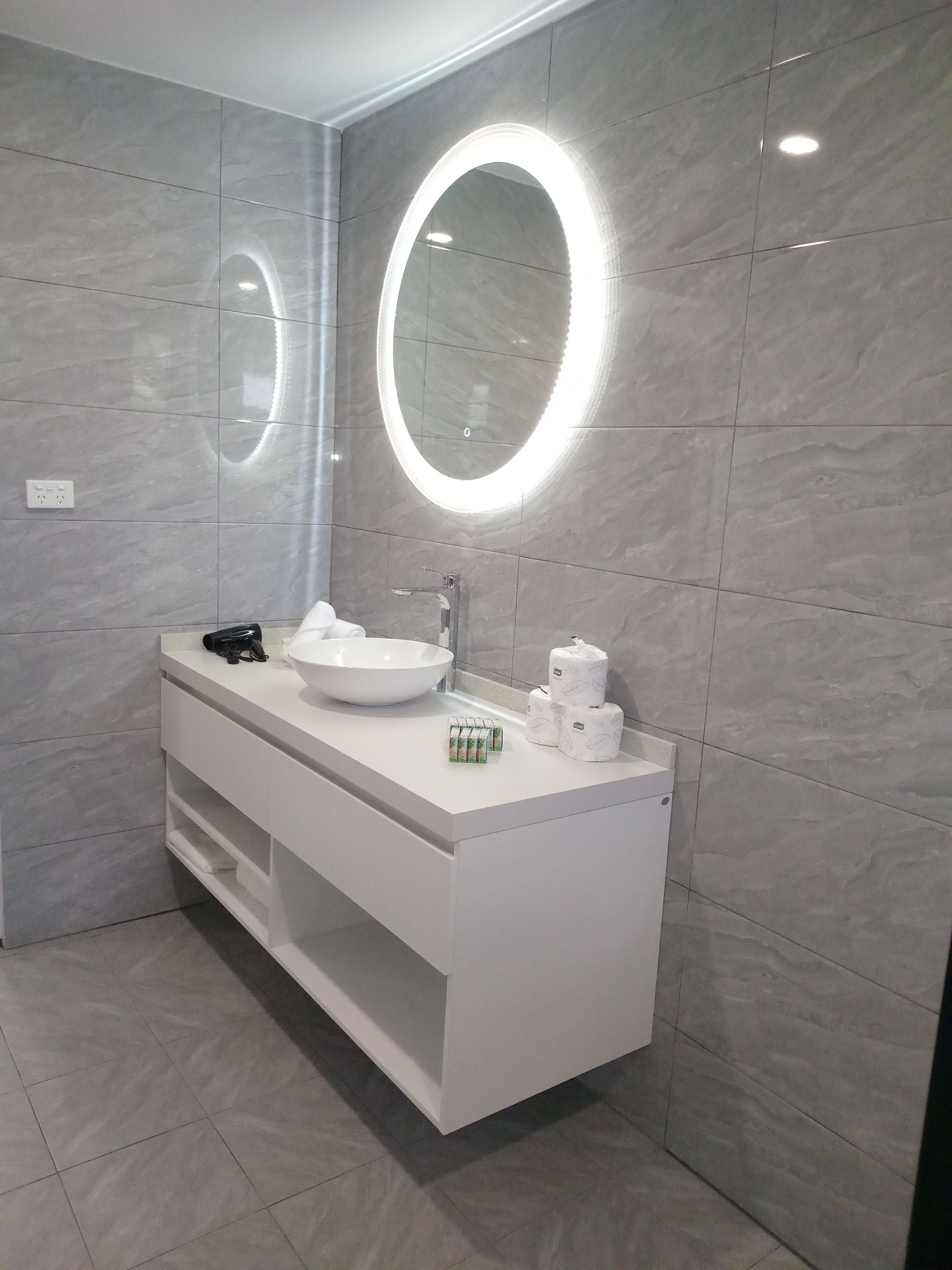 Une salle de bain moderne avec un meuble-lavabo blanc, un grand évier et deux miroirs éclairés.